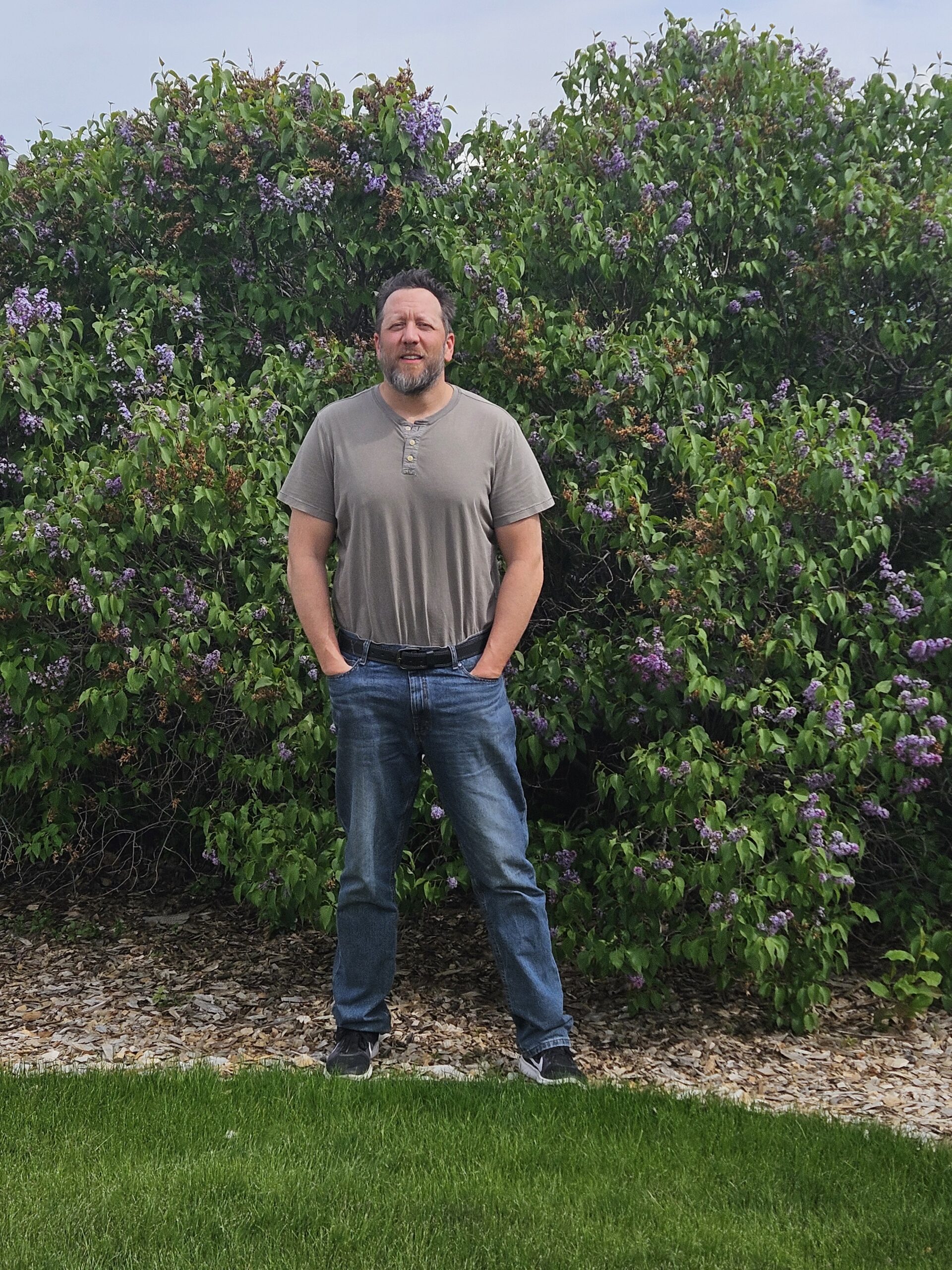 Brian Heck standing outdoors in front of dense green shrubs