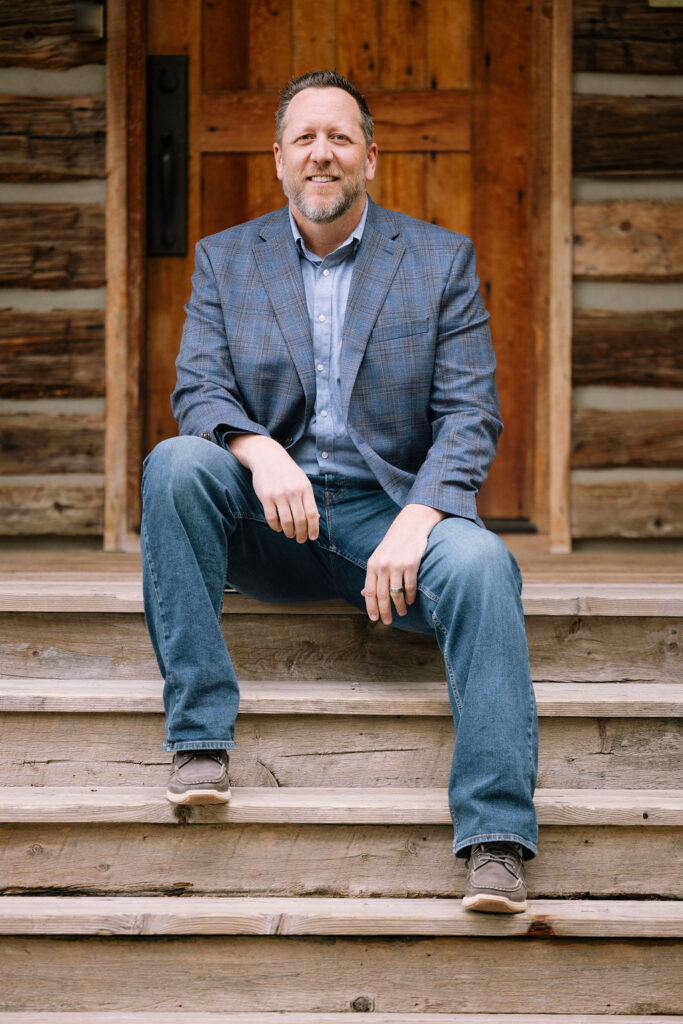 Brian Heck seated outside a rustic home in Bozeman, Montana